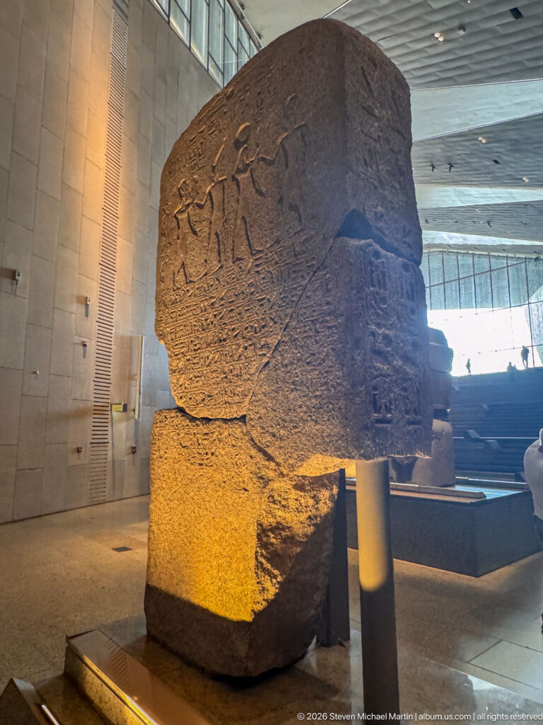 Massive broken stone block with shallow carved figures and hieroglyphic inscriptions on adjoining faces.