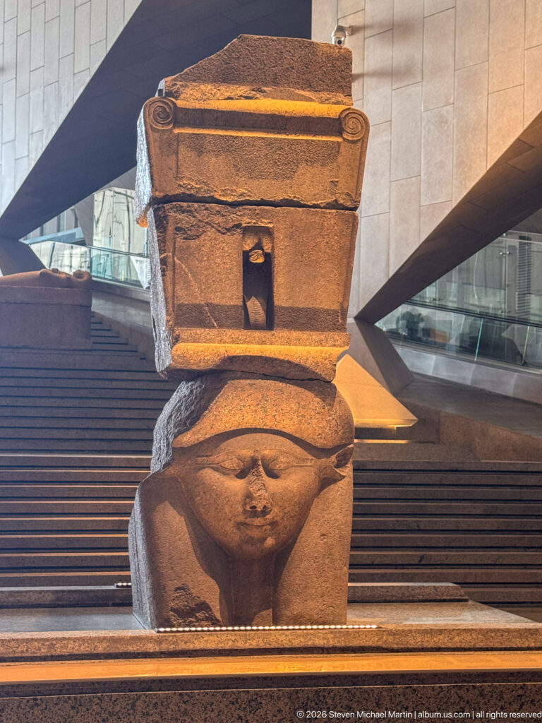 Ptolemaic red-granite Hathor capital with the goddess's frontal face beneath a shrine-shaped naos.