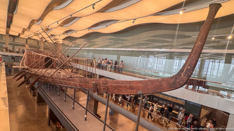 Full side view of King Khufu's First Boat, showing its long wooden hull, high curved ends, deck structure, and steering oars.