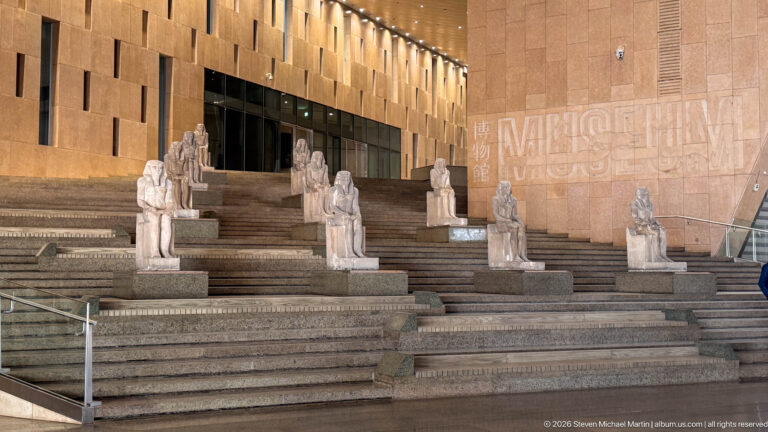Ancient Egyptian seated and standing statues arranged across broad granite terraces of the Grand Staircase.