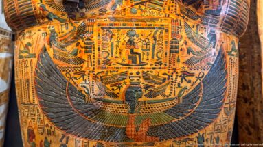 Painted coffin detail with a central winged goddess, spread feathers, hieroglyphs, and surrounding funerary figures.