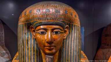 Close-up of an anthropoid coffin face with outlined eyes, striped wig, and banded headdress.