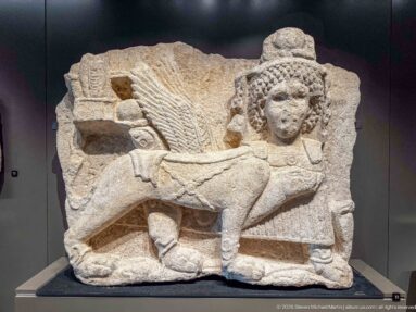 Fragmentary limestone relief with a human figure in profile, textured hair, draped clothing, and a bent leg.