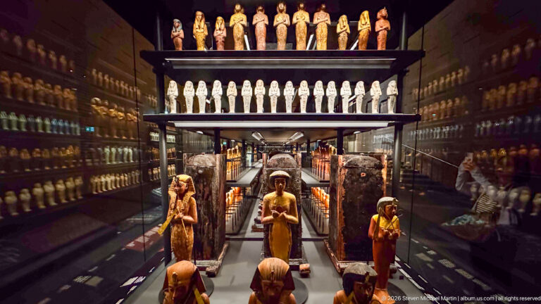 Deep gallery view through rows of shabtis and larger funerary figures, with tall dark burial objects forming a central corridor.