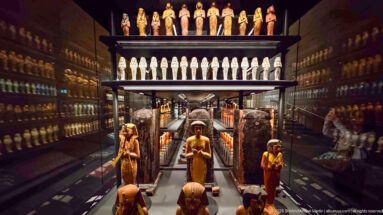 Deep gallery view through rows of shabtis and larger funerary figures, with tall dark burial objects forming a central corridor.