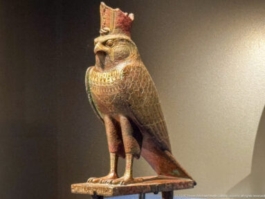 Painted falcon statuette with hooked beak, patterned plumage, and tall red-and-white double crown.