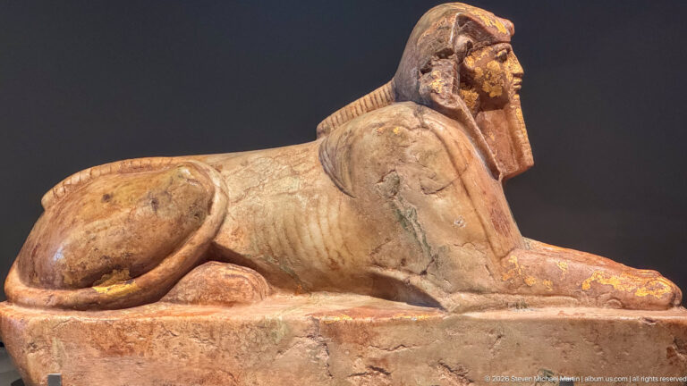 Stone sphinx with human head, striped royal headdress, lion body, and extended forepaws.