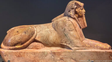 Stone sphinx with human head, striped royal headdress, lion body, and extended forepaws.