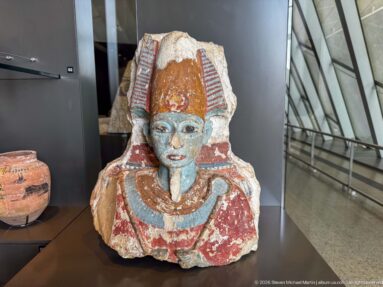Painted ancient Egyptian male head-and-torso fragment with striped headdress and broad collar.