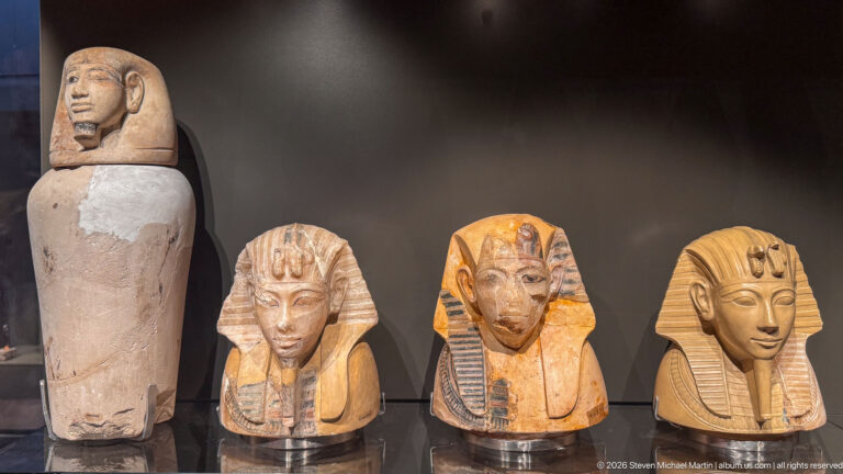 Four small ancient Egyptian funerary heads or mask-like objects displayed together, three with striped headdresses.
