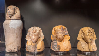 Four small ancient Egyptian funerary heads or mask-like objects displayed together, three with striped headdresses.
