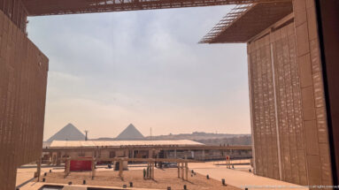 Two Giza pyramids framed between monumental museum walls above the Grand Egyptian Museum forecourt.