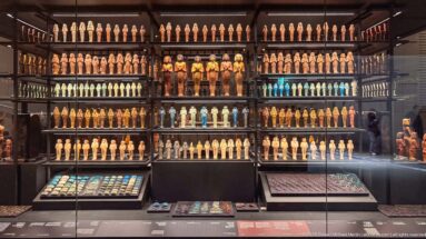 Large museum wall display packed with rows of shabtis and funerary figures, with smaller amulet trays in the foreground.
