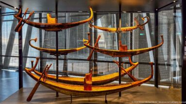Multiple ancient Egyptian wooden model boats displayed at different heights, with long narrow hulls and high curved ends.