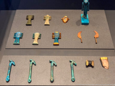 Close display of assorted ancient Egyptian protective amulets in blue-green, cream, orange, and metallic tones.