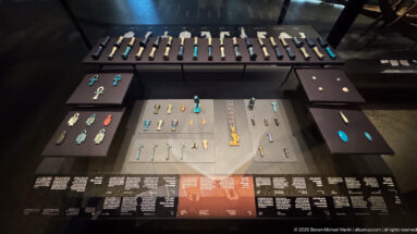 Display case with many small Egyptian amulets and pendants arranged on dark panels, including ankhs, figures, and turquoise pieces.