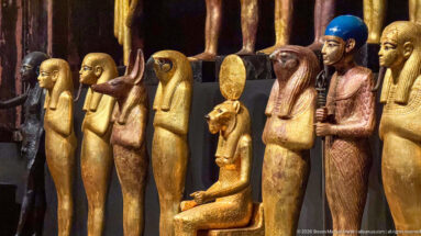 Close grouping of gilded Egyptian deities with falcon, canine, and human heads, including one seated figure beneath a solar disk.