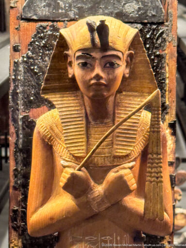 Close-up of a gilded anthropoid funerary figure with broad collar, idealized face, and crossed regalia over the chest.