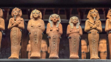 Row of anthropoid shabti figures with crossed arms, varied headdresses, and vertical inscriptions on their bodies.