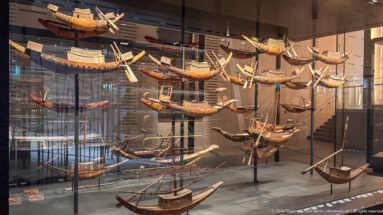Large glass museum case filled with many ancient Egyptian wooden model boats displayed at multiple heights with oars, cabins, and masts.