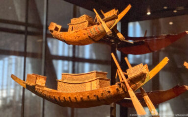 Two ancient Egyptian wooden model boats with curved hulls, patterned cabins, long oars, and painted geometric decoration.