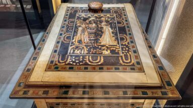 Top view of an inlaid chest lid with two standing figures facing each other amid floral motifs and multicolored geometric borders.