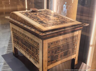 Rectangular ancient Egyptian chest on short legs with richly inlaid animal scenes and geometric borders across lid and sides.
