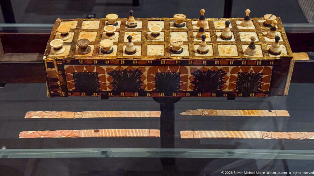 Decorated rectangular game board with a square grid, many spool- and cone-shaped playing pieces, and patterned side panels.
