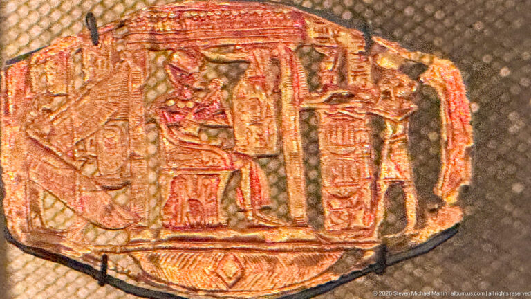 Small embossed gold plaque with multiple standing figures beneath a shrine-like architectural frame and traces of red color.