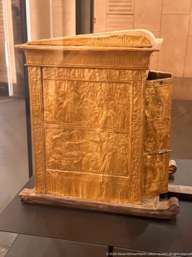 Gold-covered rectangular shrine or chest with embossed figural relief scenes, decorative borders, and projecting base supports.