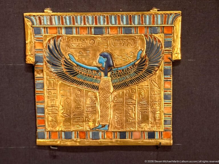 Rectangular gold panel with central winged goddess, hieroglyphic columns, cartouches, and blue-red-turquoise inlaid border.