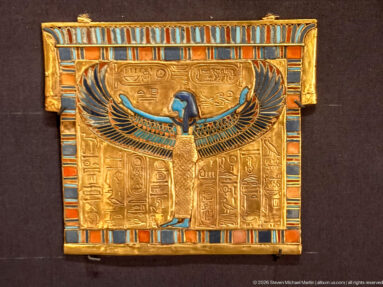 Rectangular gold panel with central winged goddess, hieroglyphic columns, cartouches, and blue-red-turquoise inlaid border.