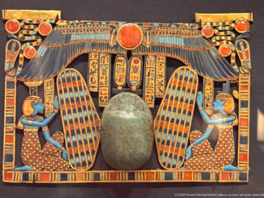 Rectangular inlaid pectoral with large green scarab, winged solar disk, kneeling figures, hieroglyphic columns, and cartouches.