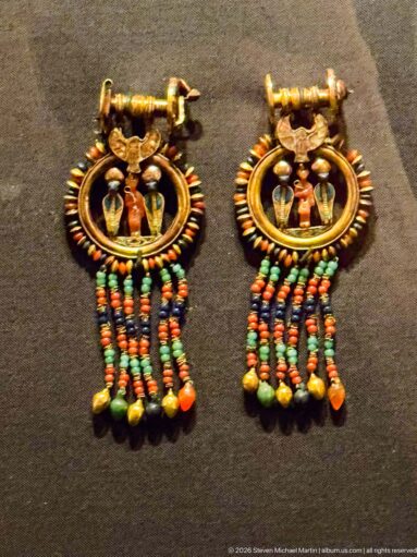 Pair of gold hoop earrings with small central amulets and several multicolored bead strands forming a fringe beneath each hoop.