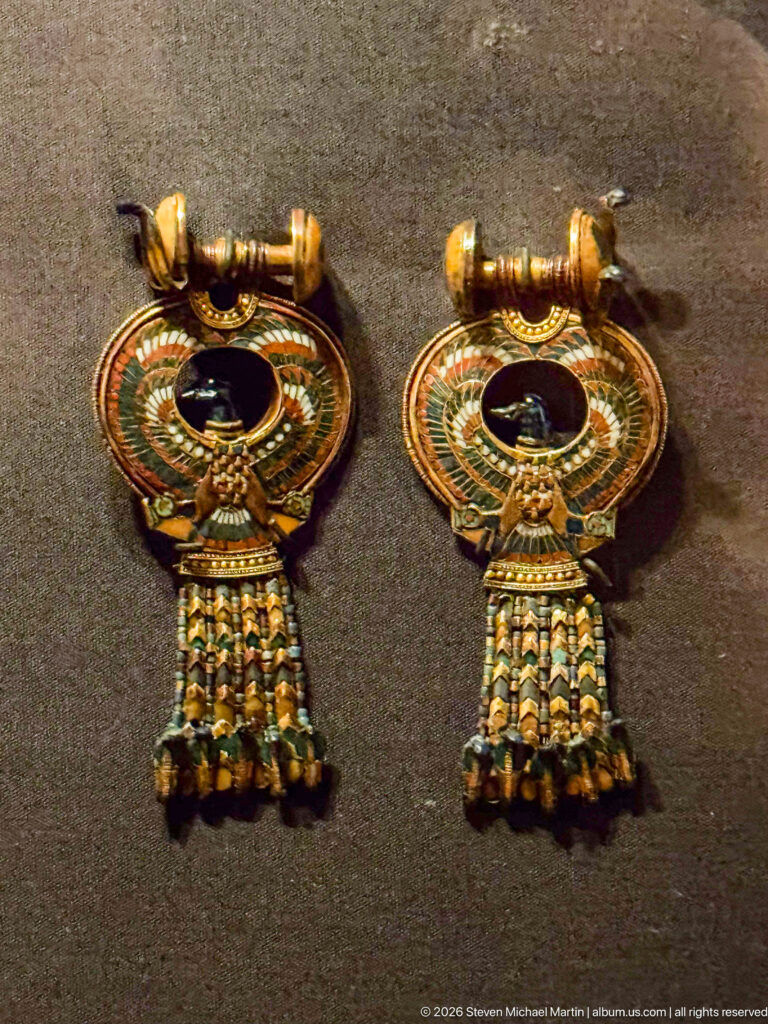 Pair of matching gold earrings with circular inlaid centers and short multicolored beaded tassels hanging below.