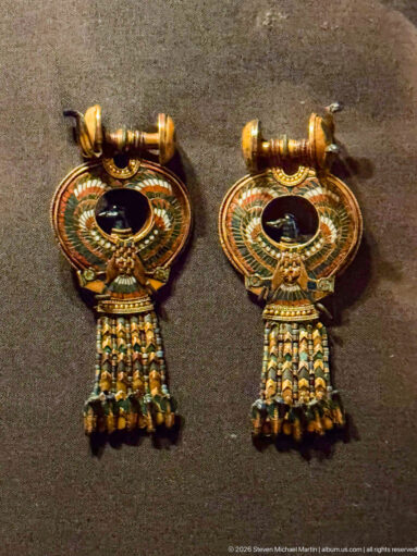Pair of matching gold earrings with circular inlaid centers and short multicolored beaded tassels hanging below.