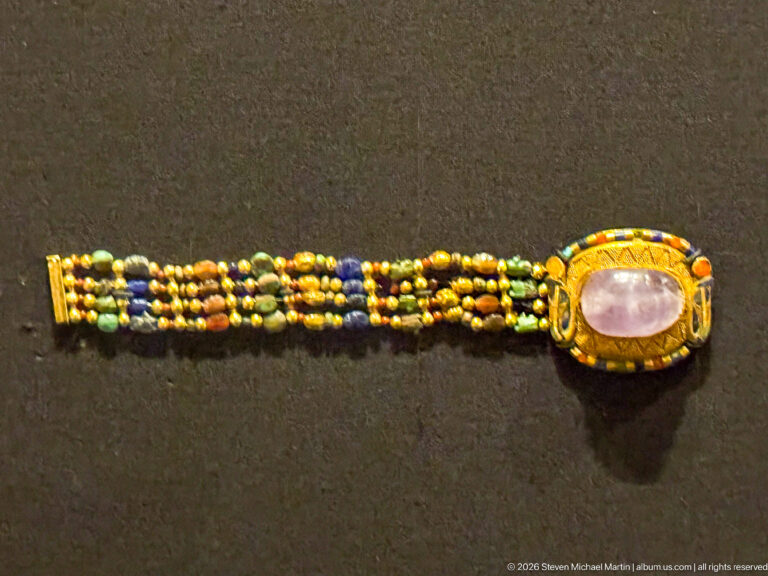 Multistrand bracelet of small colored beads with a large oval pale-violet stone set in a gold bezel at one end.
