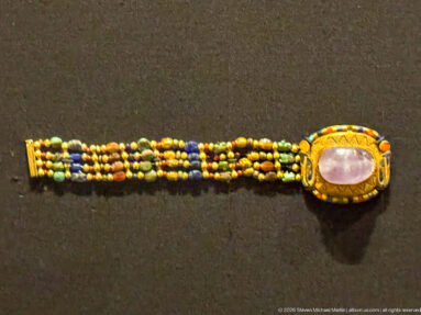 Multistrand bracelet of small colored beads with a large oval pale-violet stone set in a gold bezel at one end.