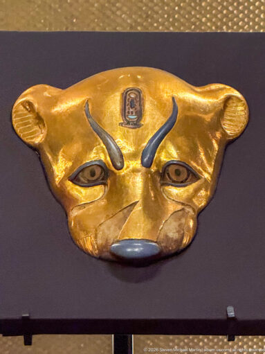 Gold feline face with broad ears, inlaid eyes, dark brows and nose, and a small royal emblem centered on the forehead.