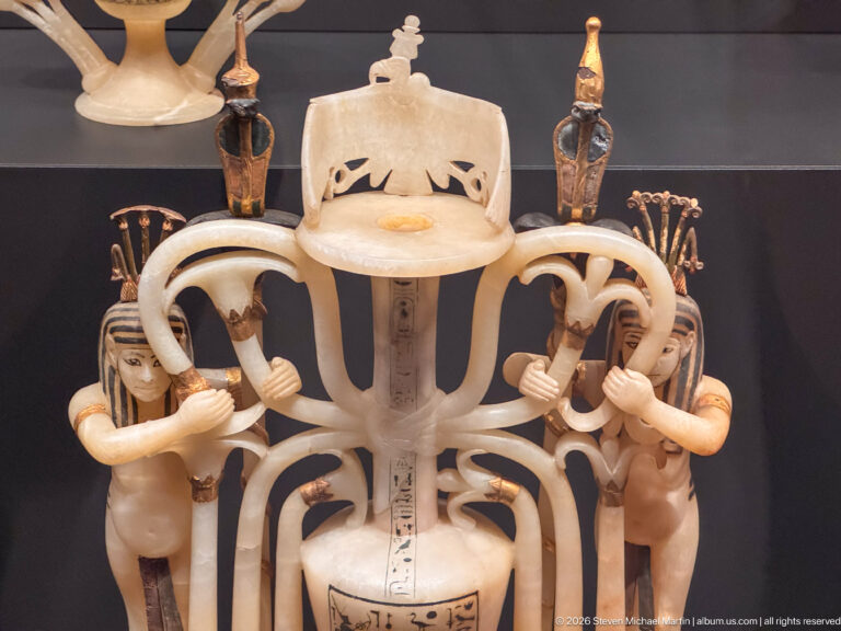 Close-up of an openwork pale stone ritual vessel with paired human figures, looping supports, small columns, and incised hieroglyphs.