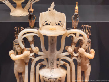 Close-up of an openwork pale stone ritual vessel with paired human figures, looping supports, small columns, and incised hieroglyphs.