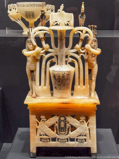 Elaborate pale stone openwork vessel with paired figures, sweeping curved supports, central inscribed cup, and cartouches.