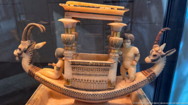 Side view of a polychrome boat-shaped vessel with ibex heads, columns, and small modeled human figures.