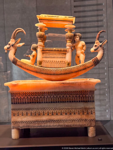 Elaborate ancient Egyptian boat-shaped vessel with ibex-head terminals, small figures, columns, and painted details.
