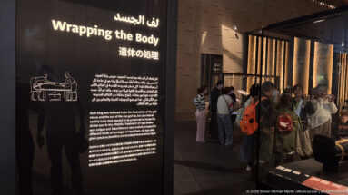 Multilingual panel titled “Preparing the Body,” with a line drawing of attendants beside a reclining body and visitors in the gallery.