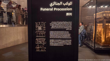 Multilingual Grand Egyptian Museum panel titled “Funeral Procession,” with explanatory text and small diagrams beside display cases.