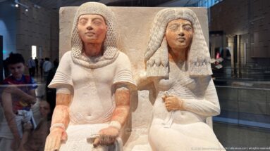 Polychrome seated couple with detailed dark wigs, white garments, red-brown skin tones, and an embracing paired pose.