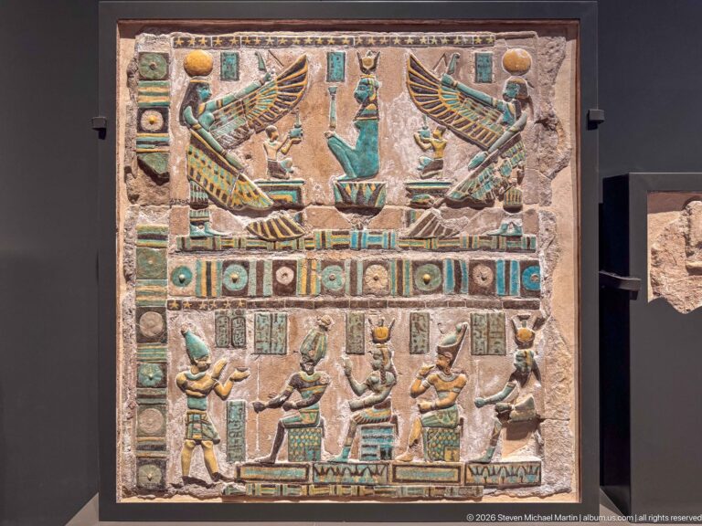 Painted Egyptian relief panel with two large winged figures above smaller ritual figures, hieroglyphs, and multicolored borders.