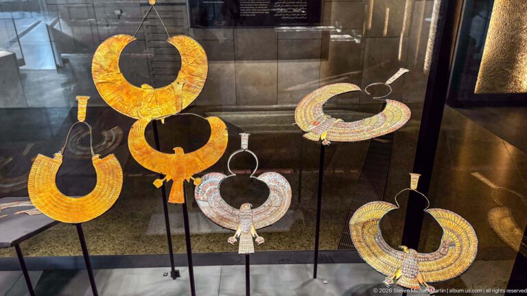 Five large gold and multicolored broad collars and pectoral necklaces mounted on black supports.
