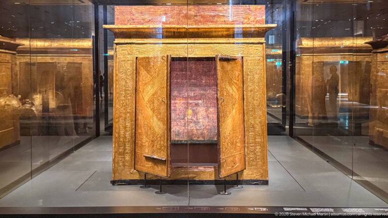 Front view of gilded shrine with two narrow open doors and a reddish inner panel.